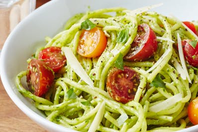 picture of bowl with pasta with avocado and sprinkled with cut up tomato