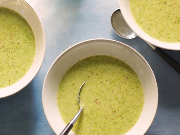 picture of bowls of bright green broccoli soup on a sky blue background