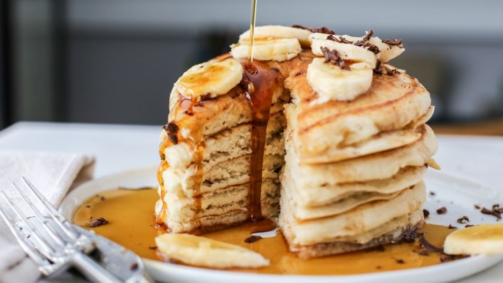 image of pancakes on a plate, topped with bananas and dripping with sweet sauce