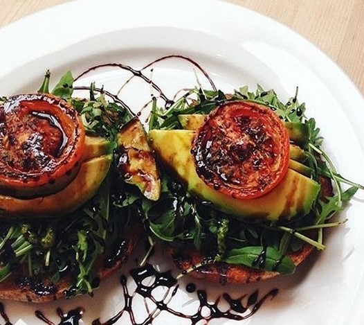 A plate of rocket, avocado and tomato toast garnished with balsamic vinegar.